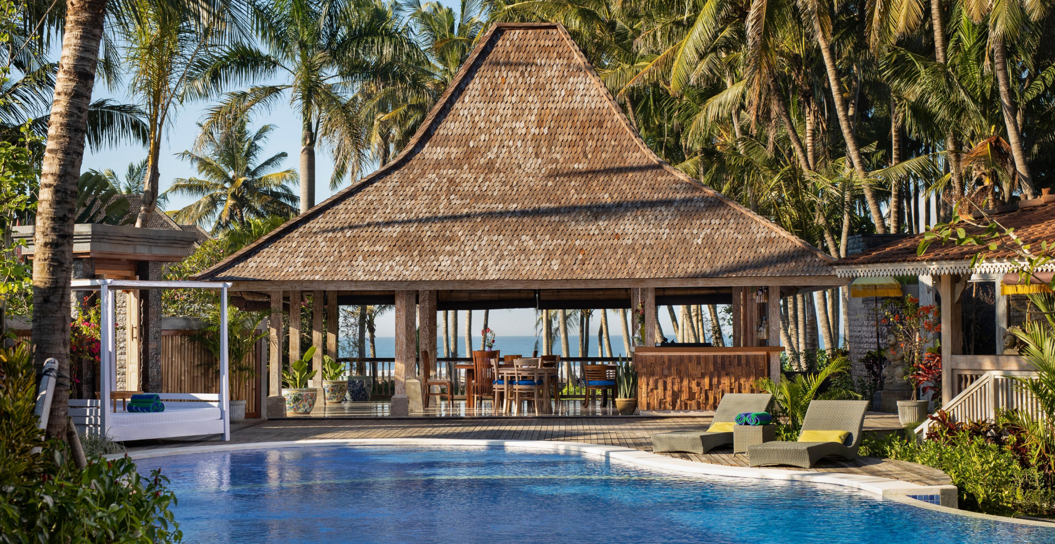 Thatched-roof poolside bar and lounge surrounded by palms at a Sanga Sanga beach resort in Bali