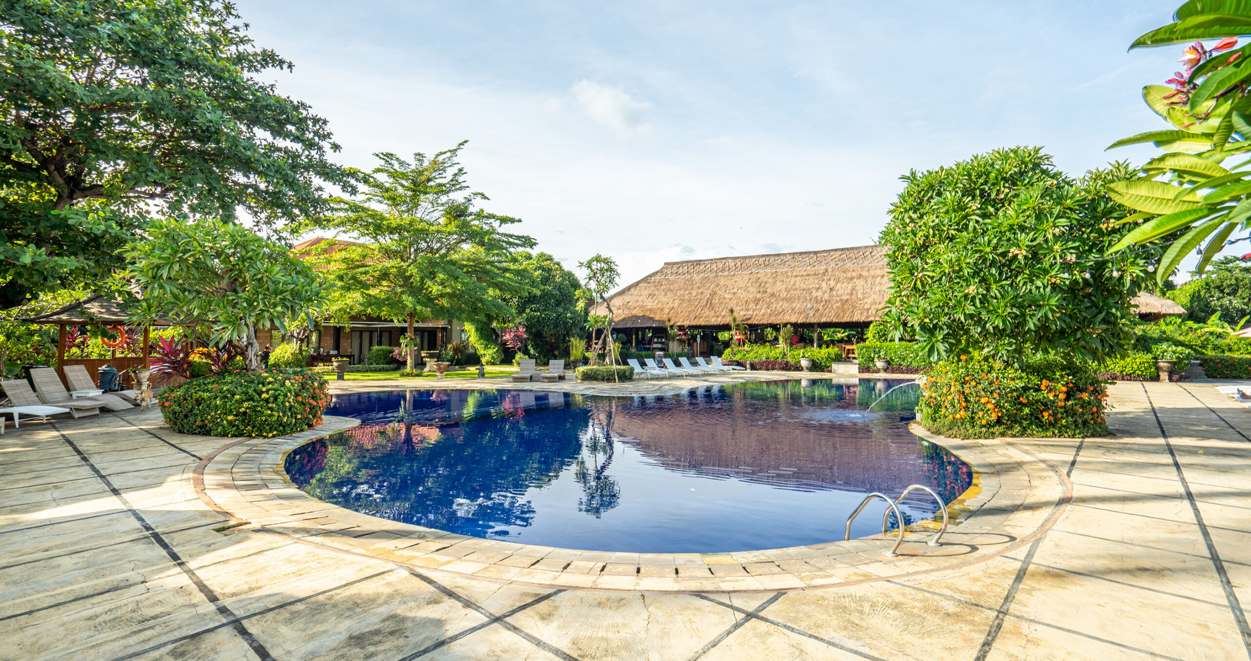 Curved resort swimming pool framed by tropical gardens and a thatched pavilion at Sanga Sanga, Bali