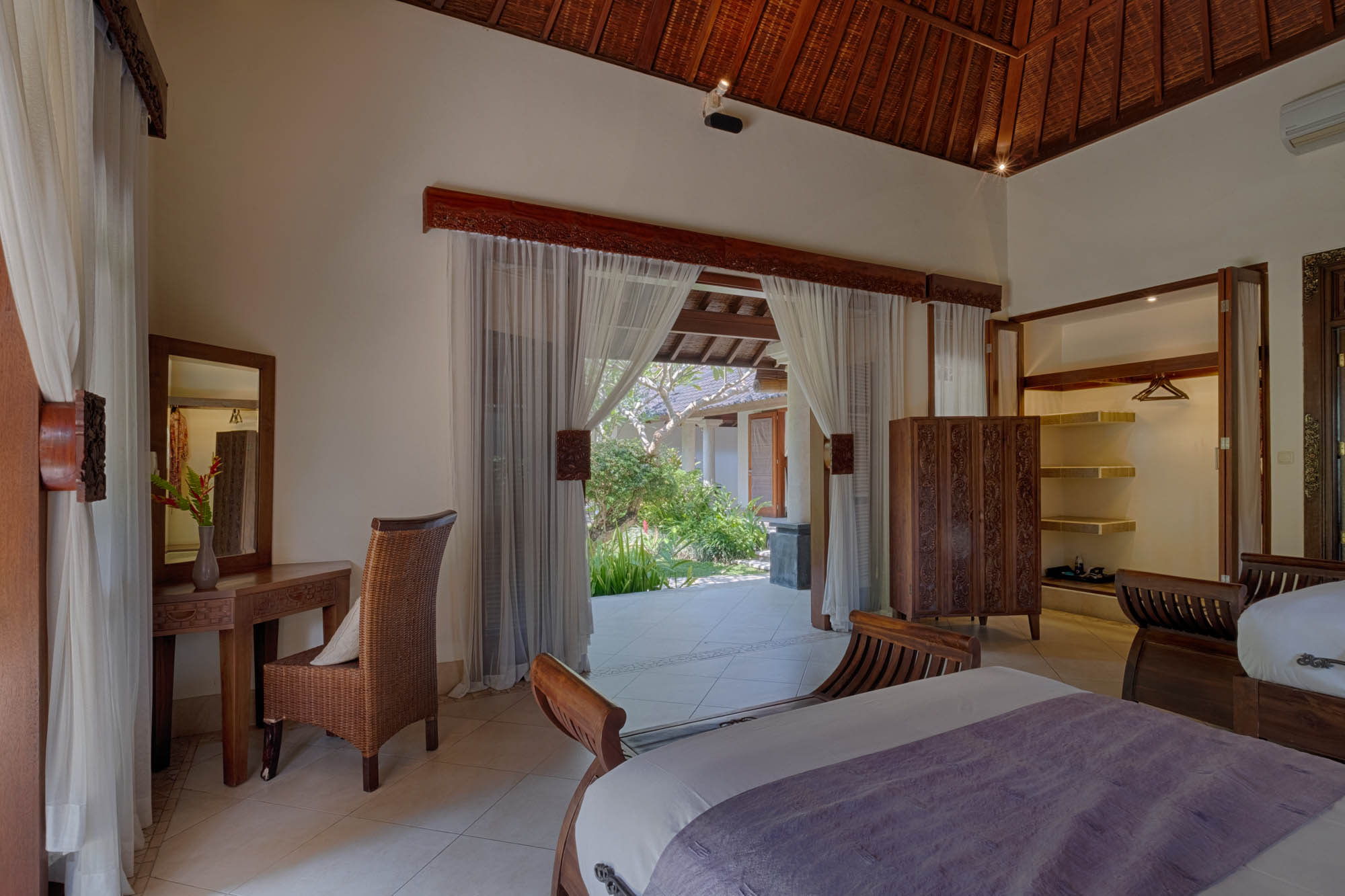 Villa bedroom with wooden vaulted ceiling and sheer-curtained doors opening to a garden at Sanga Sanga, Bali
