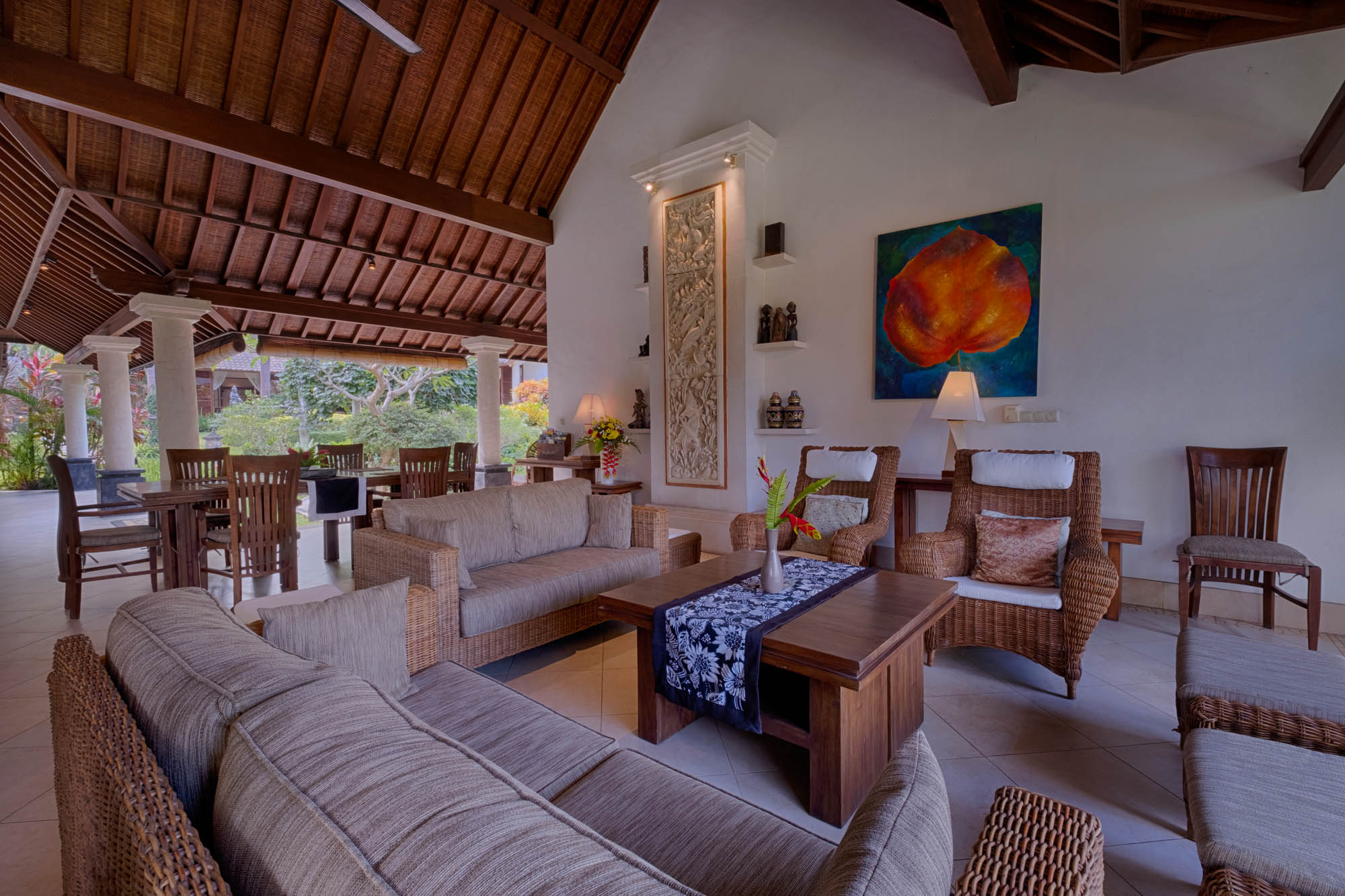 Spacious open-air lounge with woven sofas, carved Balinese accents and garden outlook at Sanga Sanga villa, Bali
