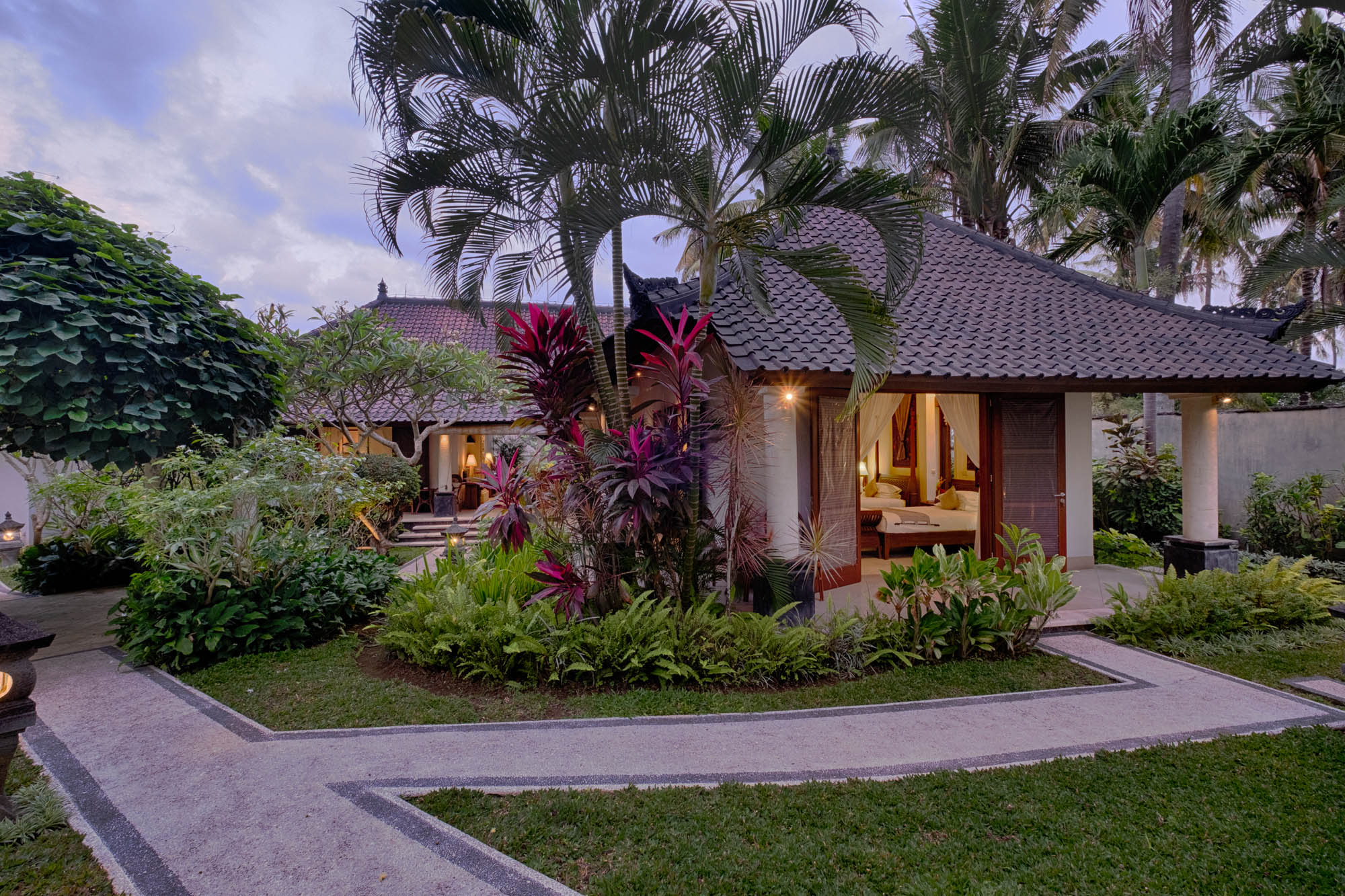 Traditional Balinese villa entrance with tiled roof and vibrant garden pathway at dusk, Sanga Sanga, Bali