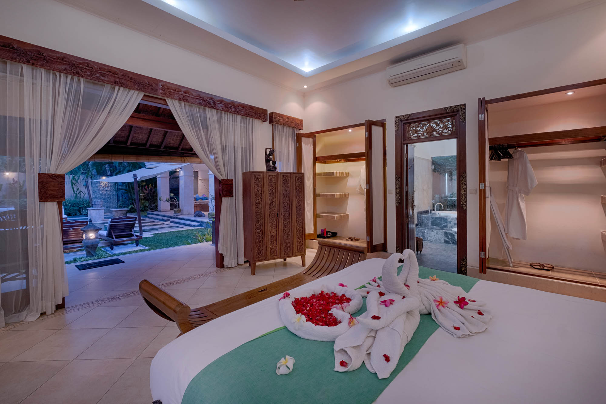 Villa bedroom with towel swan and rose petals on bed, opening to garden terrace, Sanga Sanga, Bali