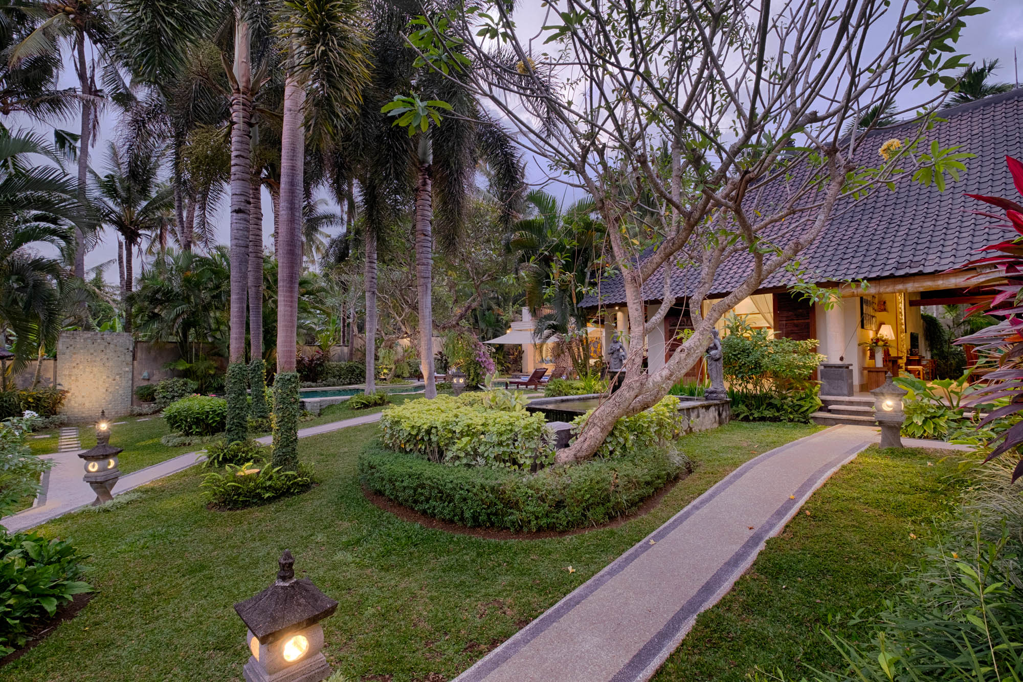 Manicured tropical garden with palms, lantern-lit pathway and villa at twilight, Sanga Sanga, Bali