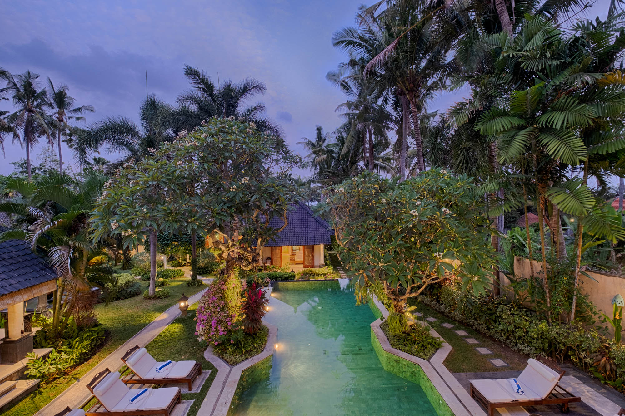 Aerial view of lush garden, pool and traditional villa lit at dusk, Sanga Sanga Hospitality, Bali